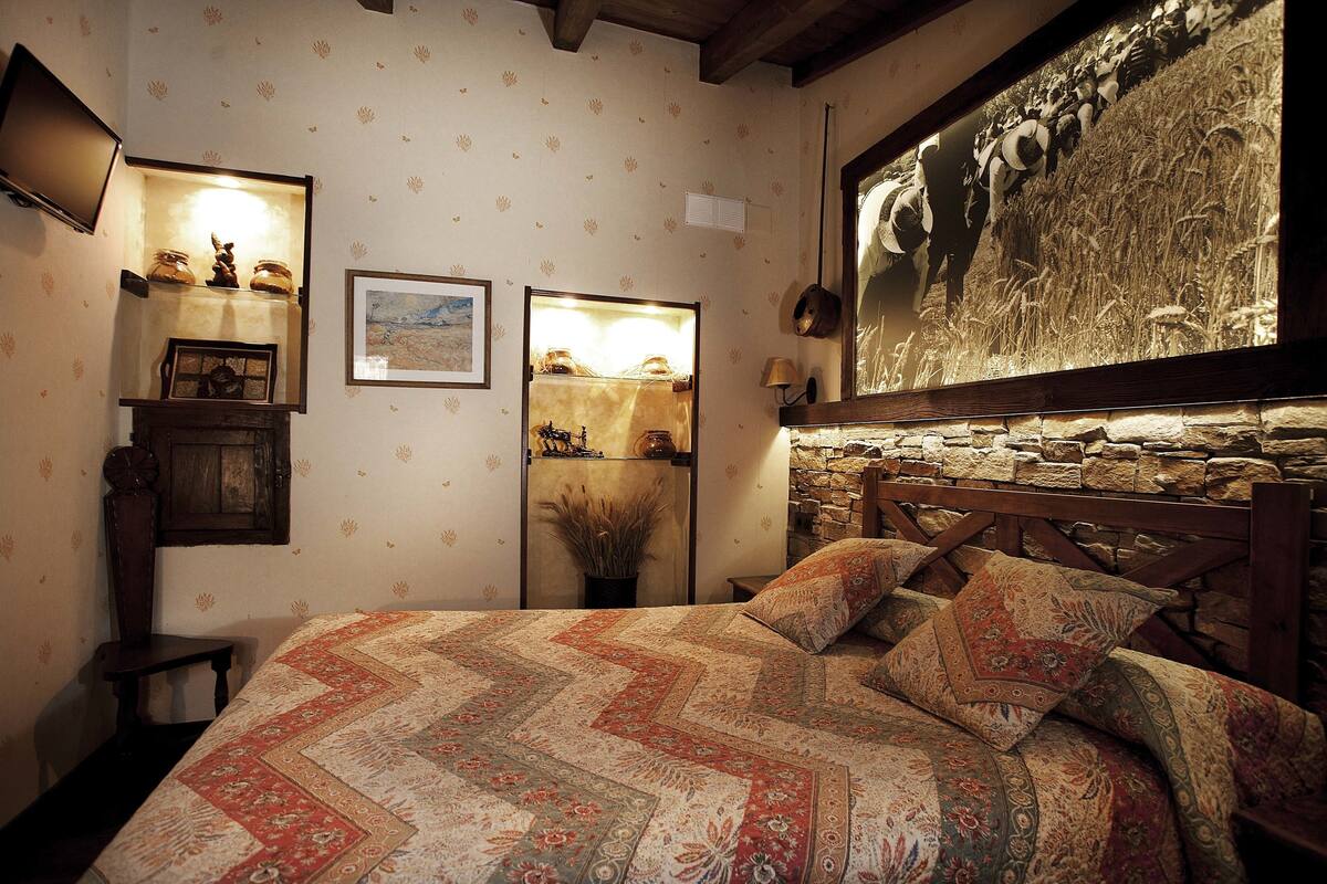 Quarto com uma cama grande, parede de pedra, televisão montada e quadro na parede.