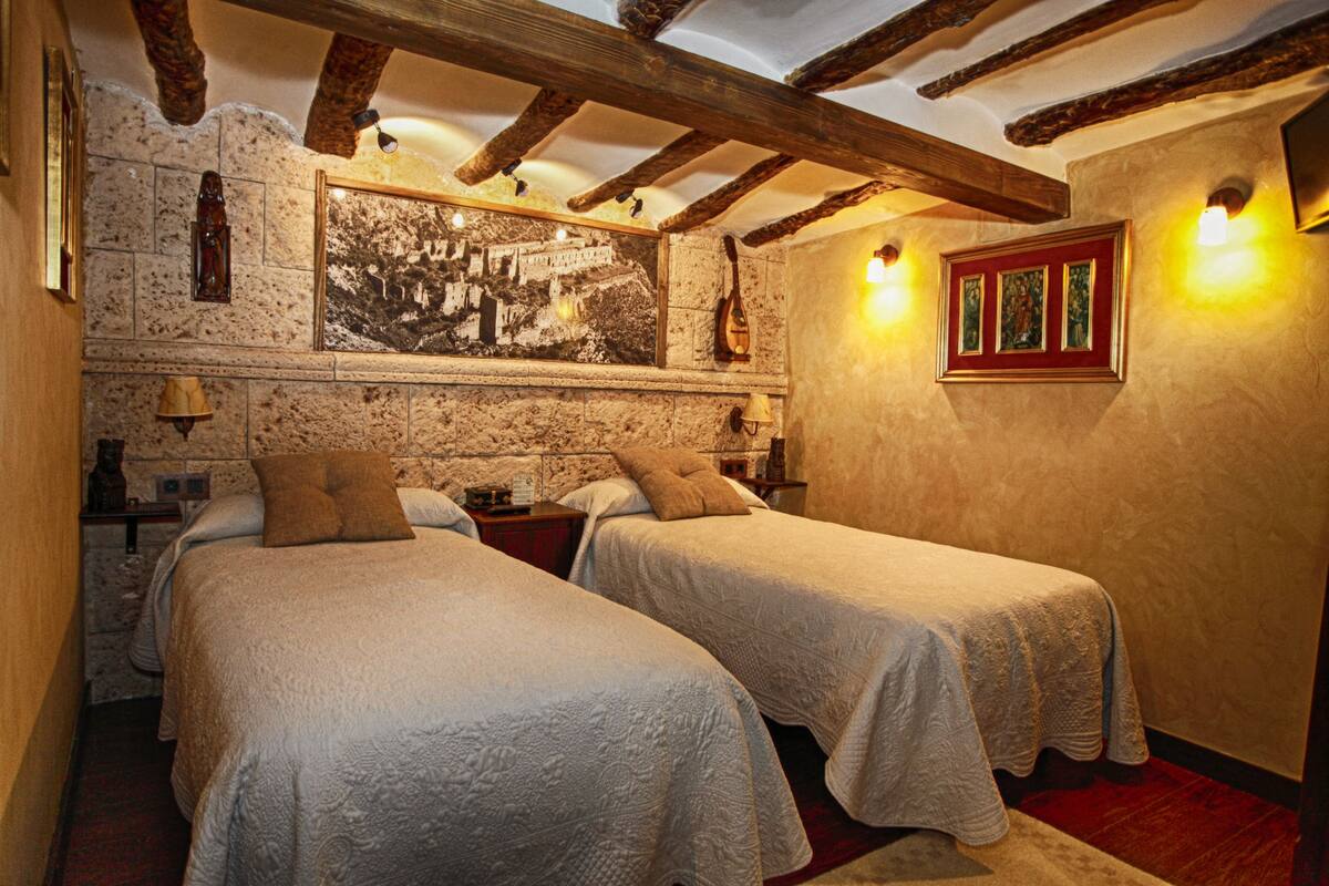 Quarto com duas camas, parede de pedra, vigas de madeira e um quadro emoldurado.