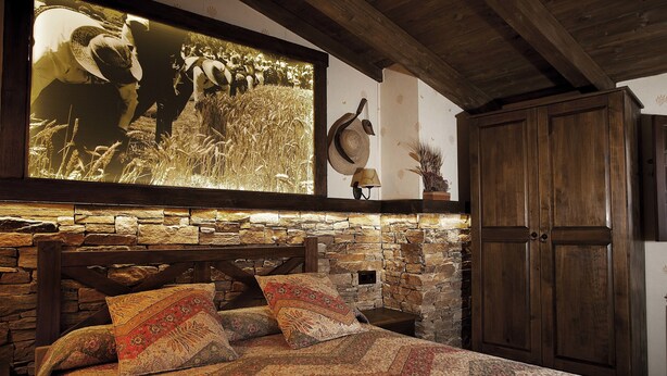 A rustic bedroom with a stone wall, wooden bed frame, and a large bedspread. - La Casa de Lucas (Clavijo)