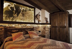 A rustic bedroom with a stone wall, wooden bed frame, and a large bedspread. - La Casa de Lucas (Clavijo)