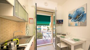 A modern kitchen with a gas stove, sink, and a dining area with a table set for two. - Fornaci 9 - 2-4 people 100 meters from the sea (Pietra Ligure)