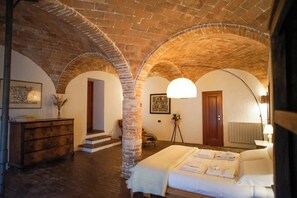 Experience the charm of a bygone era in this cozy room with exposed brick arches, a wooden bed, and a simple, functional layout.