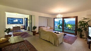 Un salón amplio con una cama grande, una zona de comedor con mesa y sillas, y vistas al exterior a través de amplias ventanas.