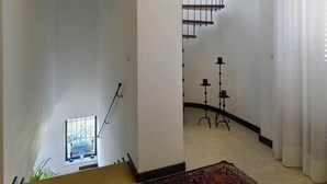 Una habitación amplia con un tapete grande estampado, una escalera que conduce a una escalera de caracol, y una ventana con vistas.
