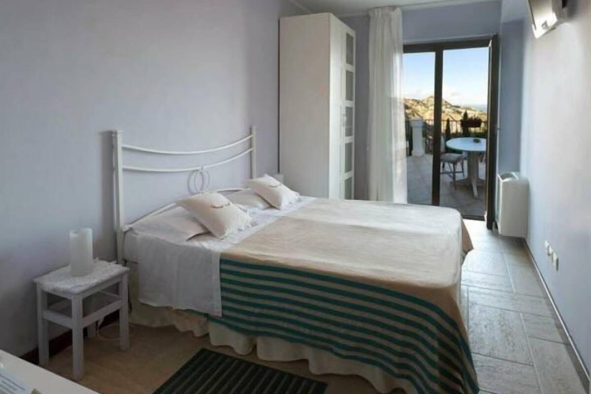 A bedroom with a bed, bedside table, and a view of the outdoors.