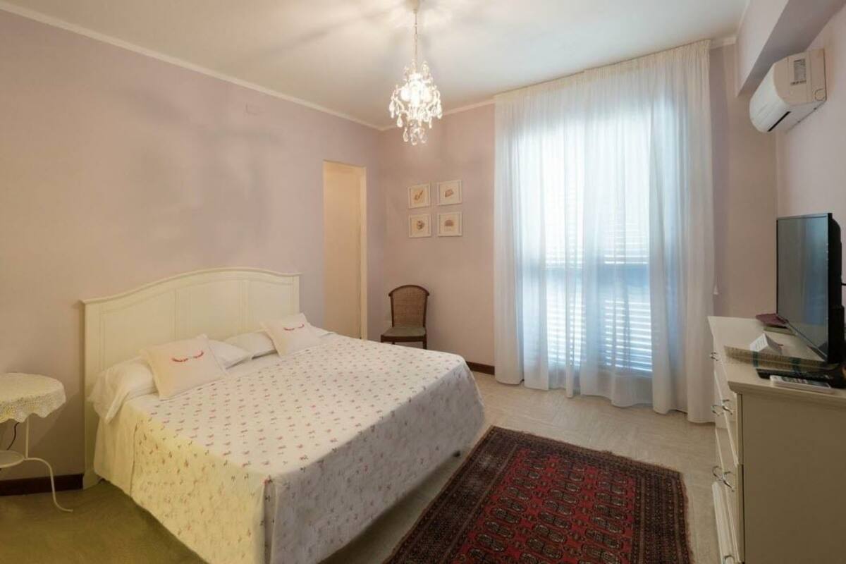 A bedroom with a bed, a chair, a small table, a TV, and a window with curtains.