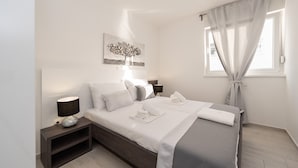 Ein modernes Schlafzimmer mit einem Bett, Nachttischen, einer Lampe und einem Fenster mit Vorhängen.