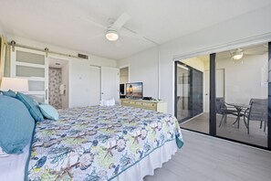 A bedroom with a bed, a television, a desk, and a sliding glass door leading to a balcony with outdoor seating. - St Pete Isla Casa C-103 2/2 Bath Amazing View! (Isla Del Sol)