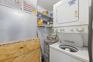 Uma lavanderia com máquina de lavar e secadora Whirlpool, aquecedor de água e prateleiras com produtos de limpeza.