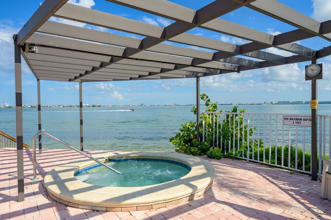 Un jacuzzi bajo una pérgola con vistas al agua y un letrero que indica una profundidad máxima de 3 pies.