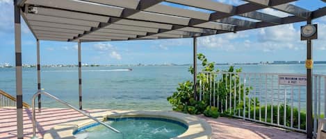 A hot tub under a pergola with a view of the water and a sign indicating a maximum depth of 3 feet.