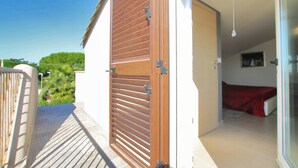 A balcony with a wooden door, a bed with a red cover, and a view of greenery. - Villa Tulipano - 2 Bathrooms Garden Wi-Fi Air Conditioing, Terrace, near the Sea (Campofelice di Roccella)