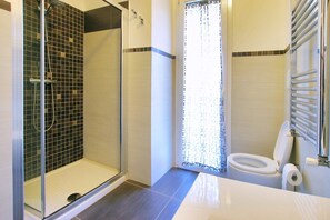 A bathroom with a glass-enclosed shower, a toilet, and a sink.
