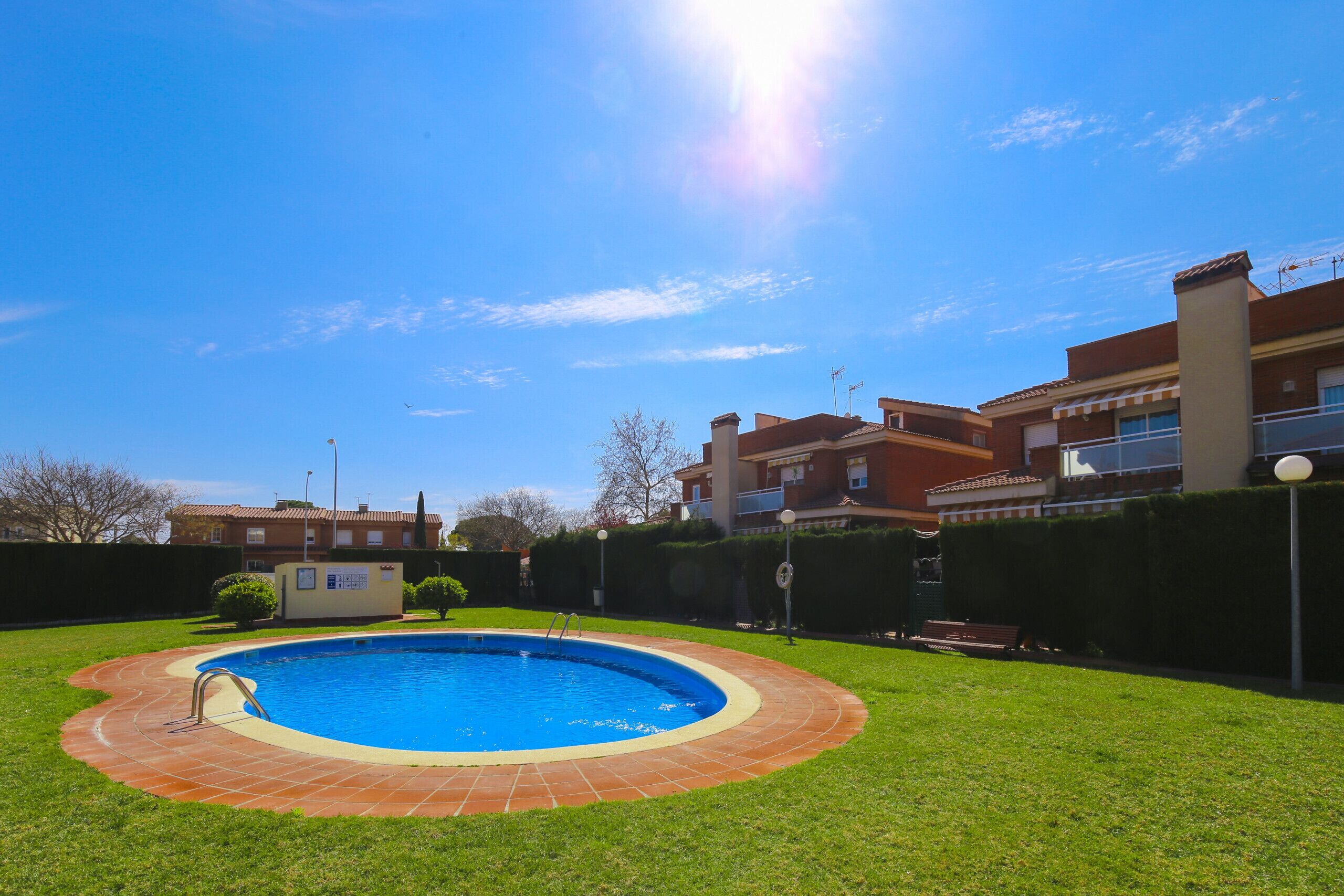 A swimming pool with a tiled edge, surrounded by a grassy lawn and a brick border.