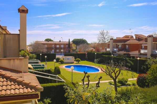 A residential area with a swimming pool surrounded by well-maintained lawns and hedges, with houses featuring tiled roofs and brick walls.