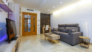Una sala de estar moderna con un sofá gris, una mesa de centro de madera, un televisor sobre un mueble de madera, una pared de piedra y una puerta de madera.