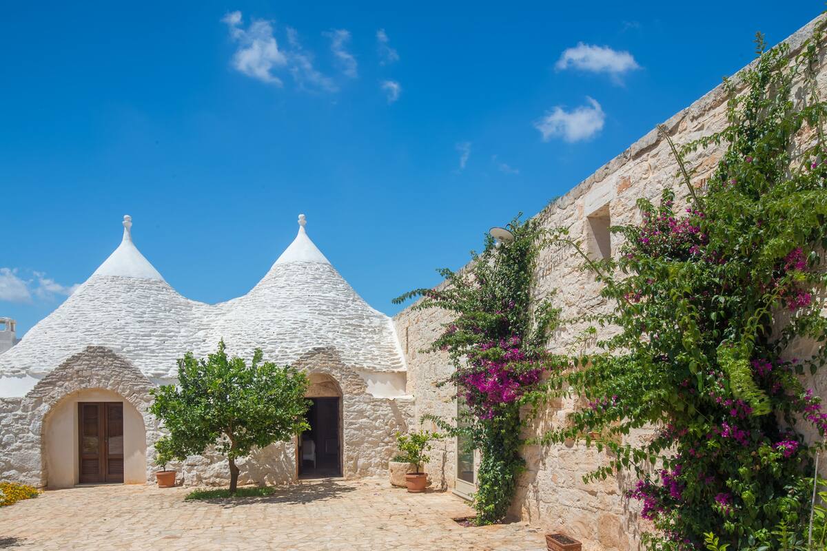 A courtyard with stone buildings, a tree, and potted plants.