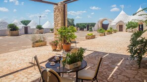 Un patio con suelo de piedra, plantas en macetas y una mesa con sillas.