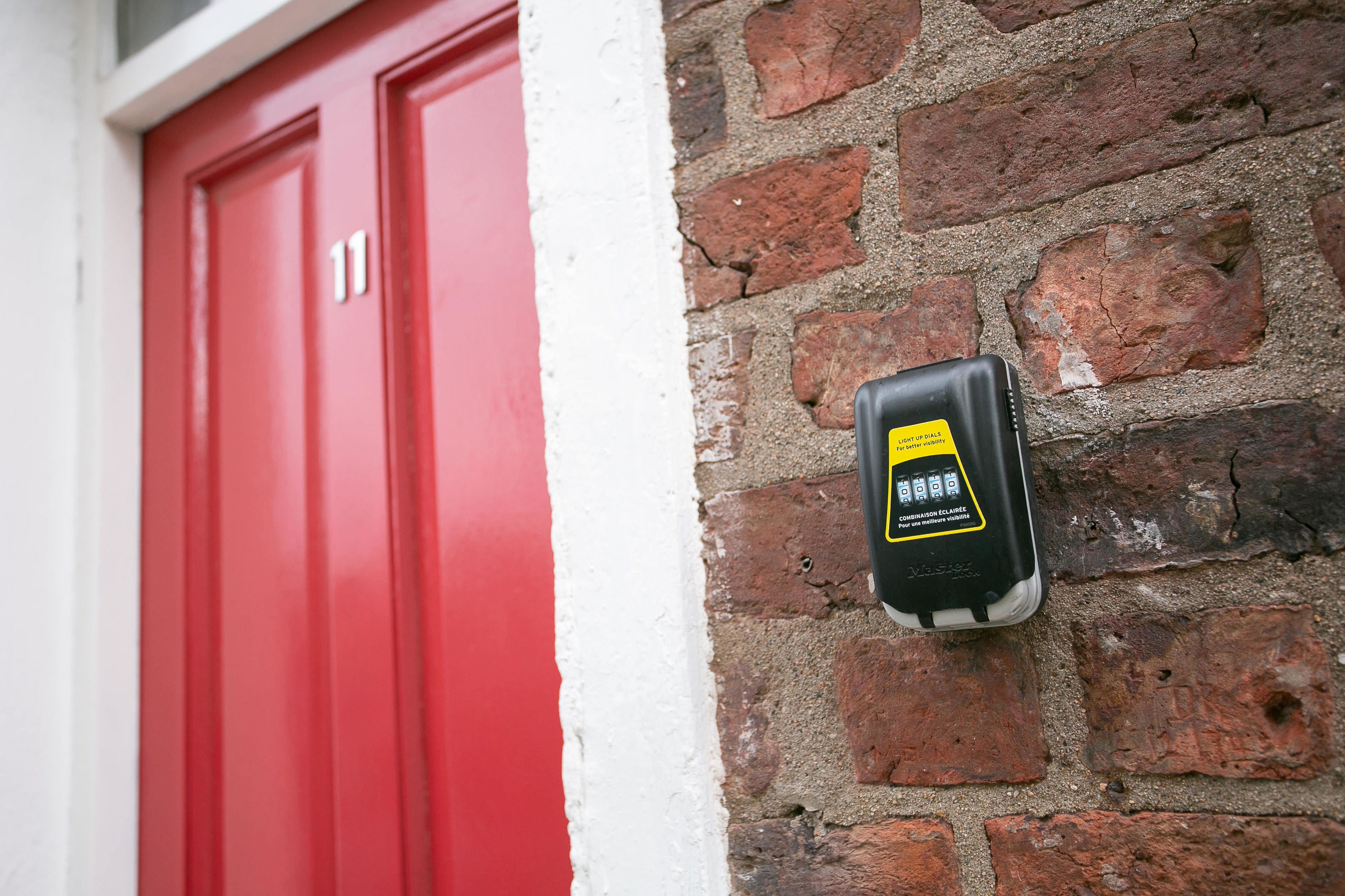 A red door with the number 11, a black device attached to a brick wall, and a white baseboard.