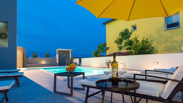 Un espace aménagé au bord de la piscine, avec des chaises longues, une table sur laquelle se trouvent une bouteille et un verre, et un parasol jaune.