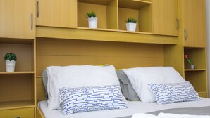 Une chambre à coucher bien rangée, avec un lit, deux oreillers, une table de chevet et une étagère ornée de plantes en pot.