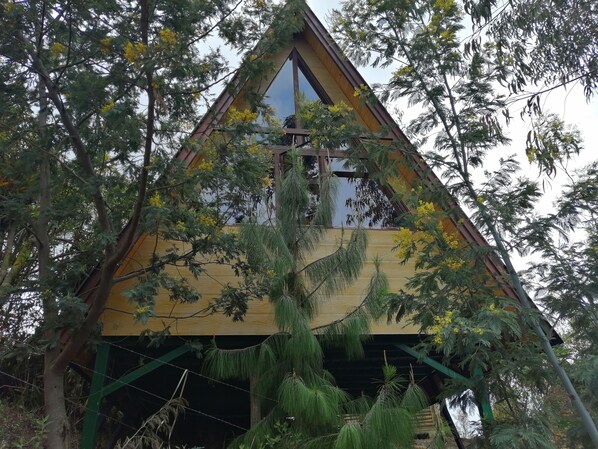 Una estructura de madera triangular con un amplio ventanal y una cruz en la parte superior.