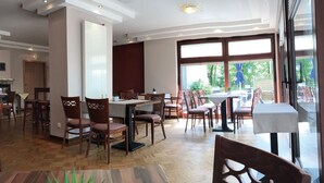 A restaurant with wooden flooring, multiple tables and chairs, and large windows offering a view of the outdoors.