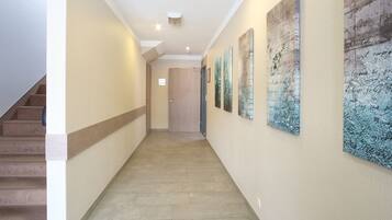 A hallway with a staircase on the left, a door at the end, and three framed artworks on the right wall.