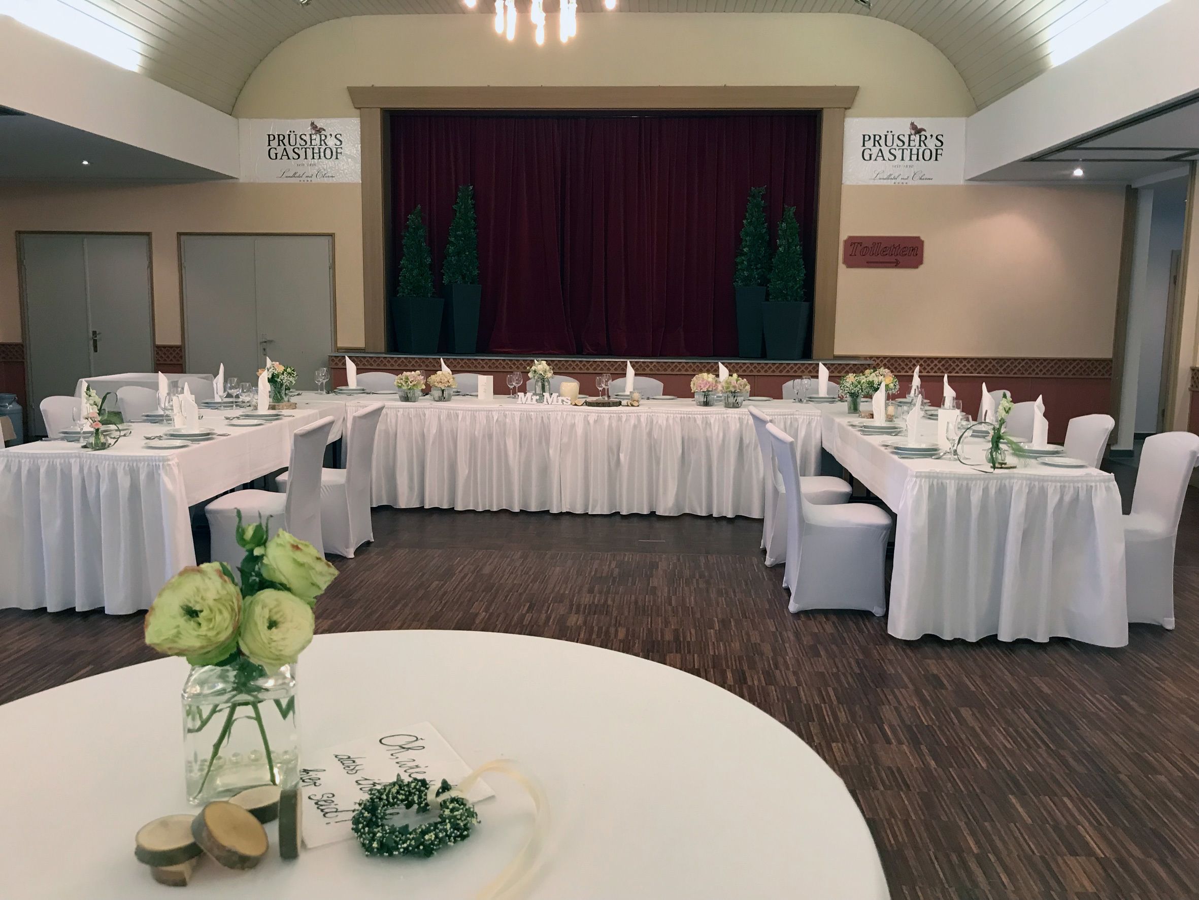 Een balzaal met meerdere ronde tafels gedekt voor een formeel evenement, met witte tafellakens en bloemstukken als decoratie.