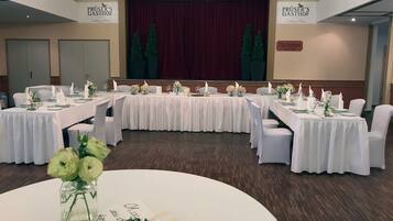 Een balzaal met meerdere ronde tafels gedekt voor een formeel evenement, met witte tafellakens en bloemstukken als decoratie.