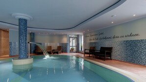A swimming pool with a water feature, seating area, and a wall with a German quote.