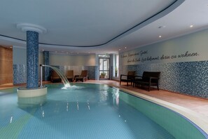 A swimming pool with a water feature, seating area, and a wall with a German quote.