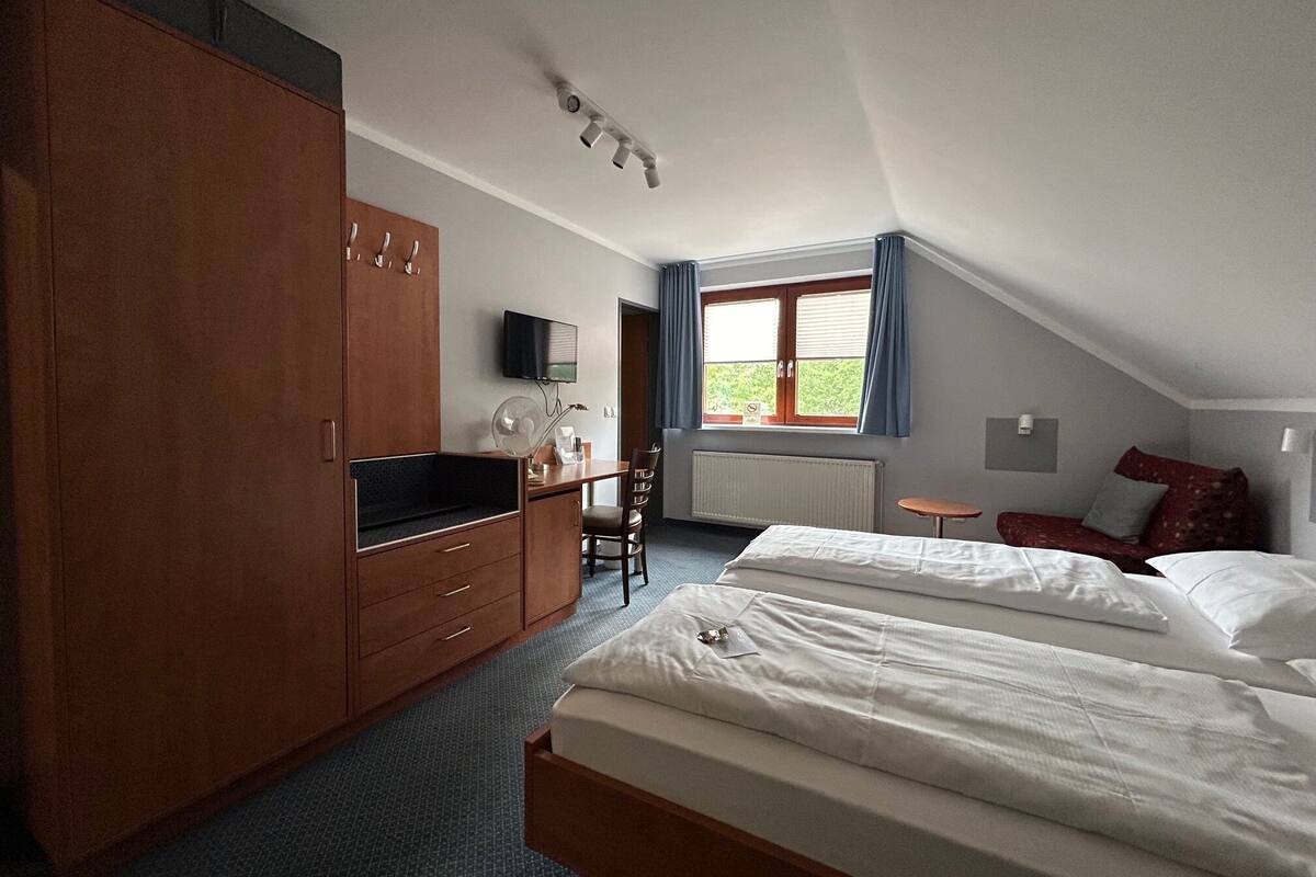 A bedroom with a bed, a desk, a chair, a wardrobe, a TV, and a window with curtains.