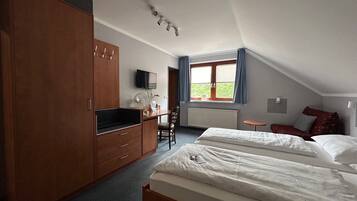A bedroom with a bed, a desk, a chair, a wardrobe, a TV, and a window with curtains.