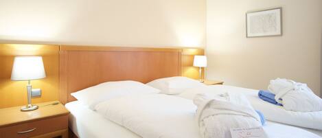 A hotel room with two beds, a wooden headboard, bedside lamps, a small table, and a welcome card.