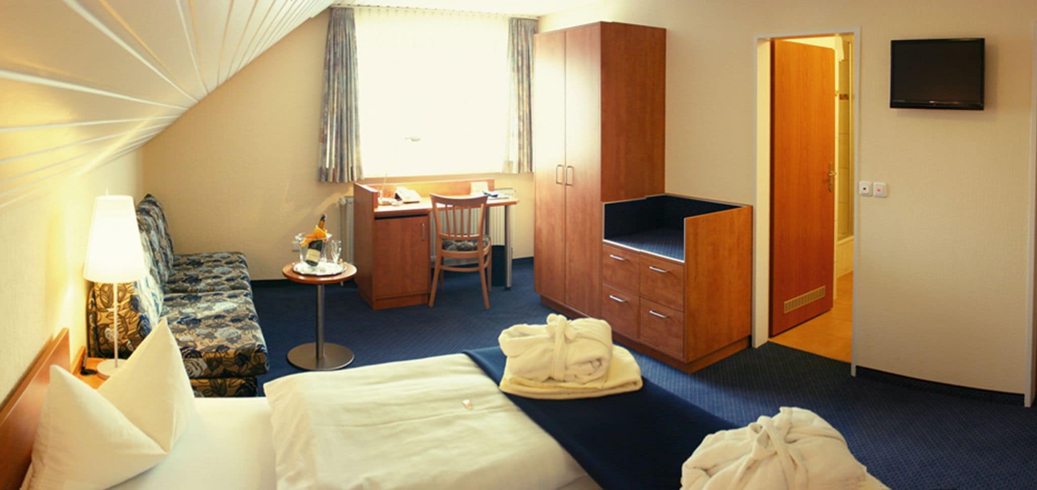 Ein Hotelzimmer mit Bett, Schreibtisch, Stuhl, Fernseher und Kleiderschrank.