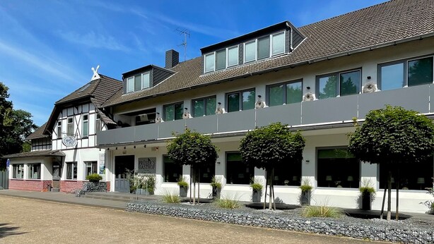 A two-story building with a modern facade, large windows, and a balcony with dogs.