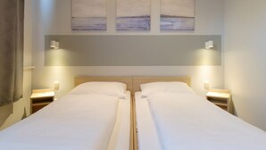 A double bed with a wooden headboard, two bedside tables with lamps, and three wall-mounted paintings above the bed.
