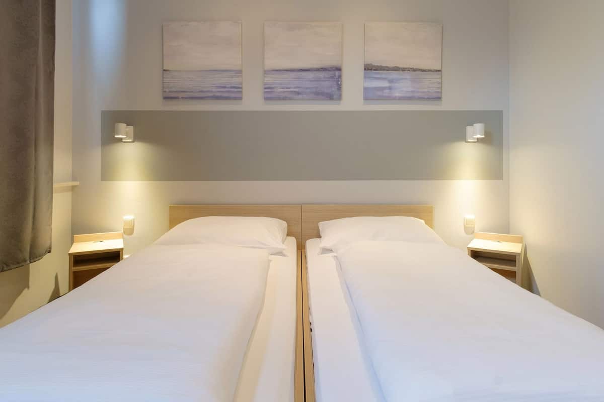 A double bed with a wooden headboard, two bedside tables with lamps, and three wall-mounted paintings above the bed.