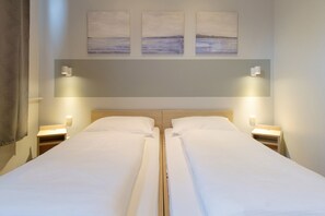A double bed with a wooden headboard, two bedside tables with lamps, and three wall-mounted paintings above the bed.