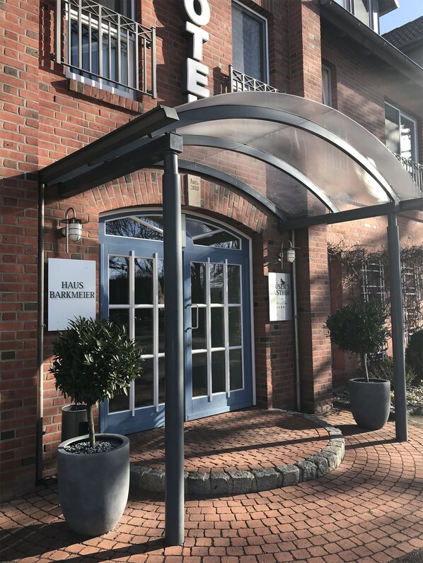 Entrada de hotel con vestíbulo cubierto, un letrero que dice 'Haus Barkmeier' y un letrero que dice 'Plüer's Gasthof'.