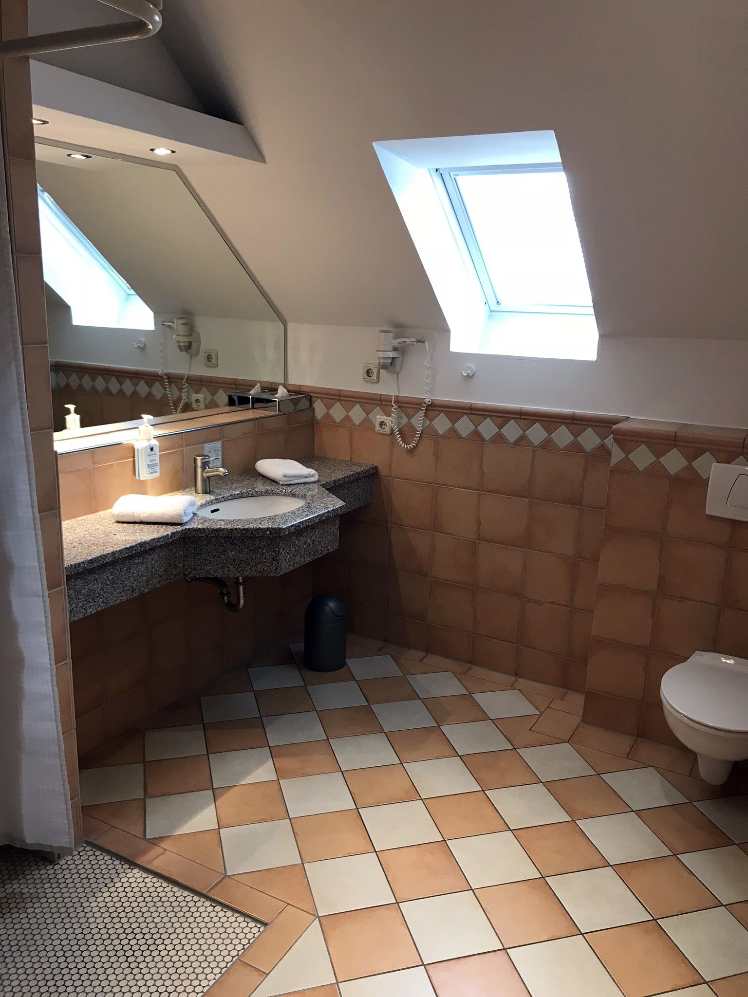 Ein kleines Badezimmer mit Oberlicht, Waschbecken, Toilette und Mülleimer.