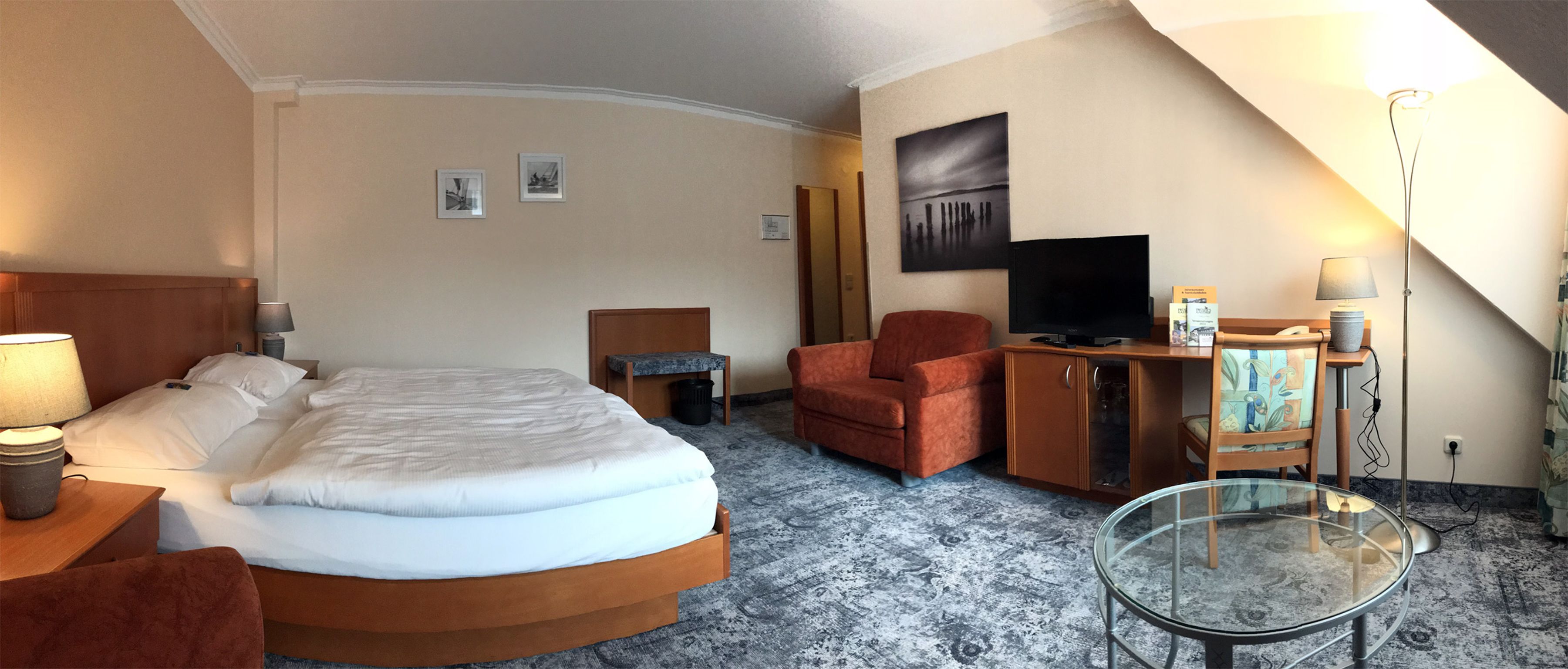 A hotel room with a bed, a desk, a chair, a TV, and a glass table.
