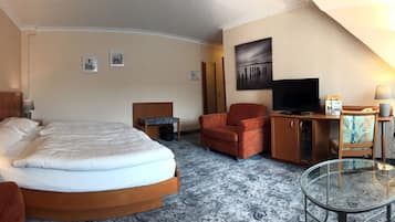 A hotel room with a bed, a desk, a chair, a TV, and a glass table.