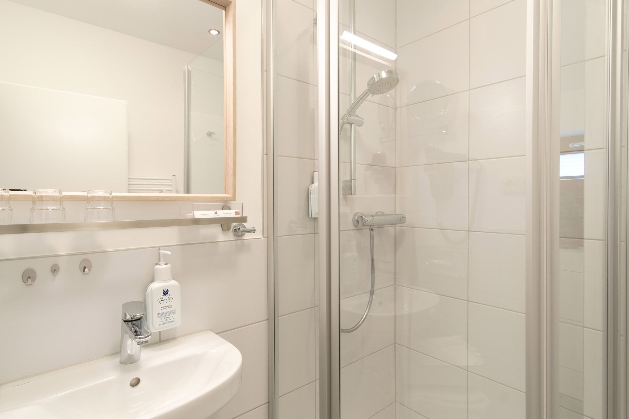 Un bany modern amb dutxa tancada amb vidre, un lavabo blanc i un mirall sobre el lavabo.