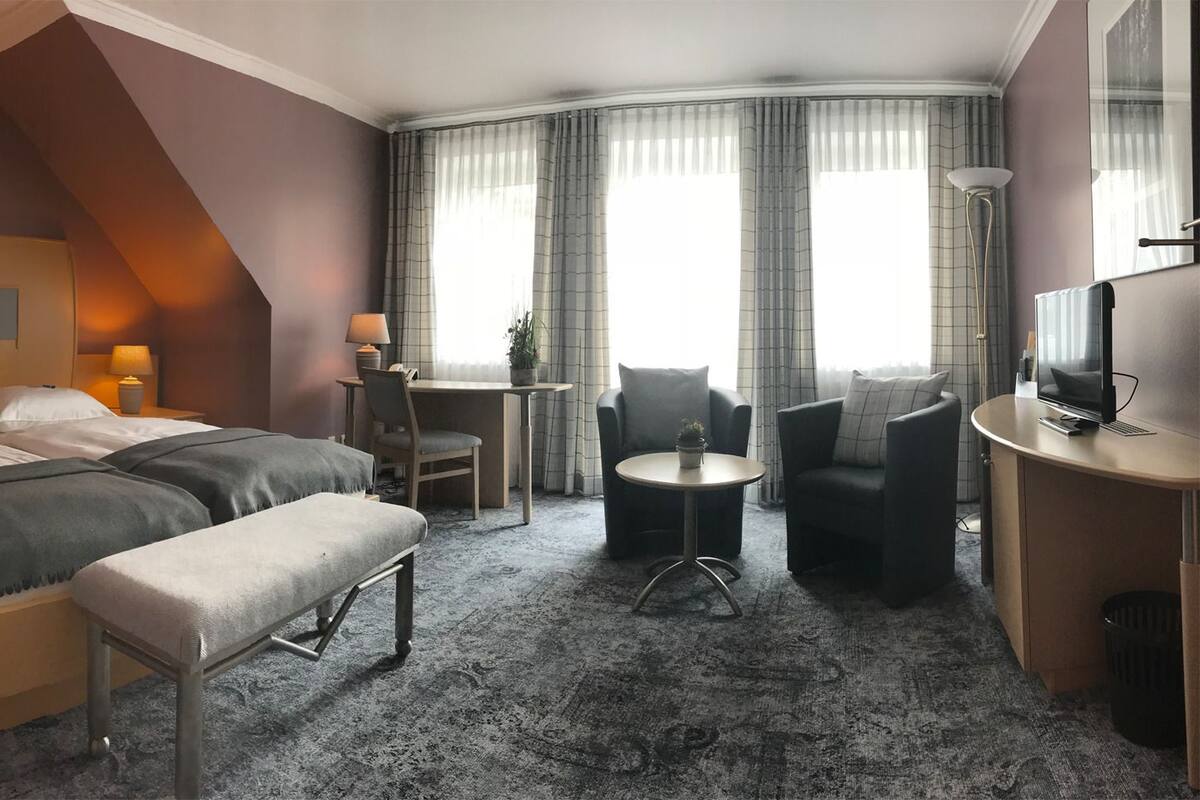 A hotel room with a large bed, a desk, a chair, and a TV.