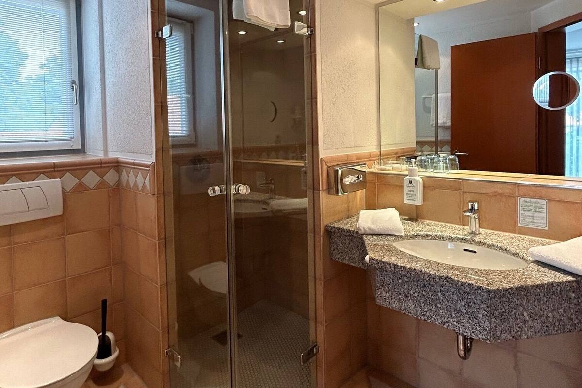A modern bathroom with a glass-enclosed shower, two sinks, and a toilet.