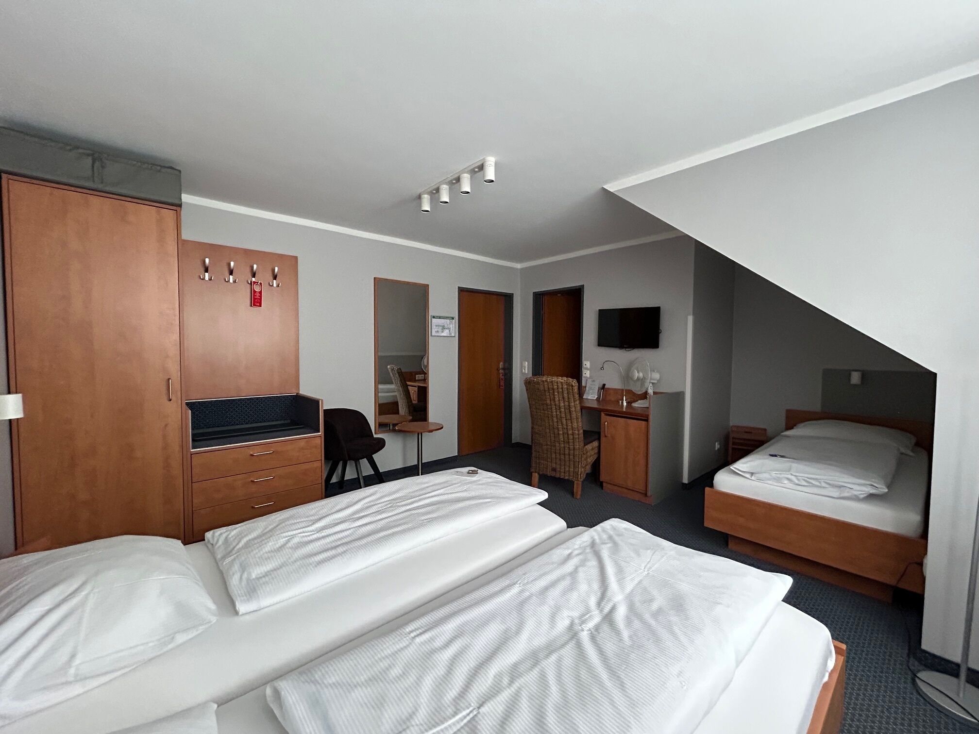 Habitación de hotel con dos camas, un escritorio, una silla, un armario y un televisor.