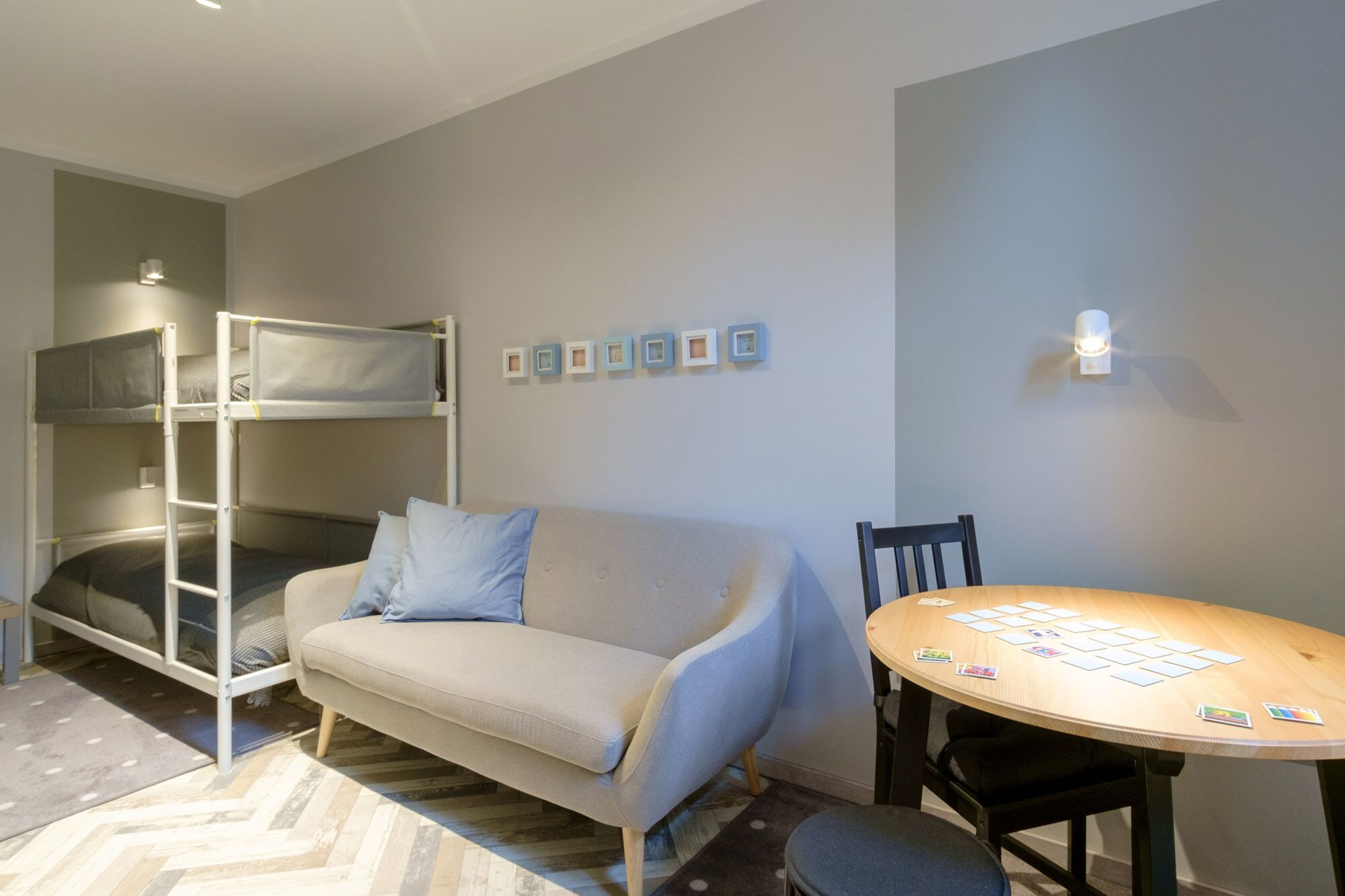 Una habitación con literas, un sofá, una mesa de comedor y una lámpara fijada a la pared.