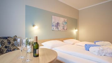 Quarto de hotel com uma cama, uma mesa redonda com duas taças de vinho e uma garrafa, e um quadro na parede.